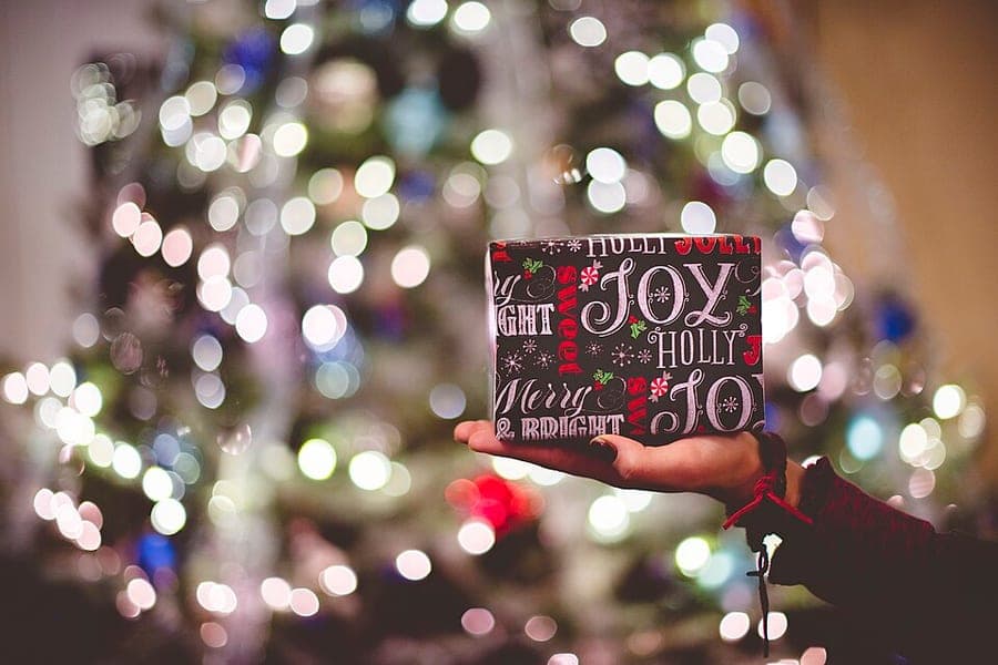 A wrapped gift held in front of a lit Christmas tree