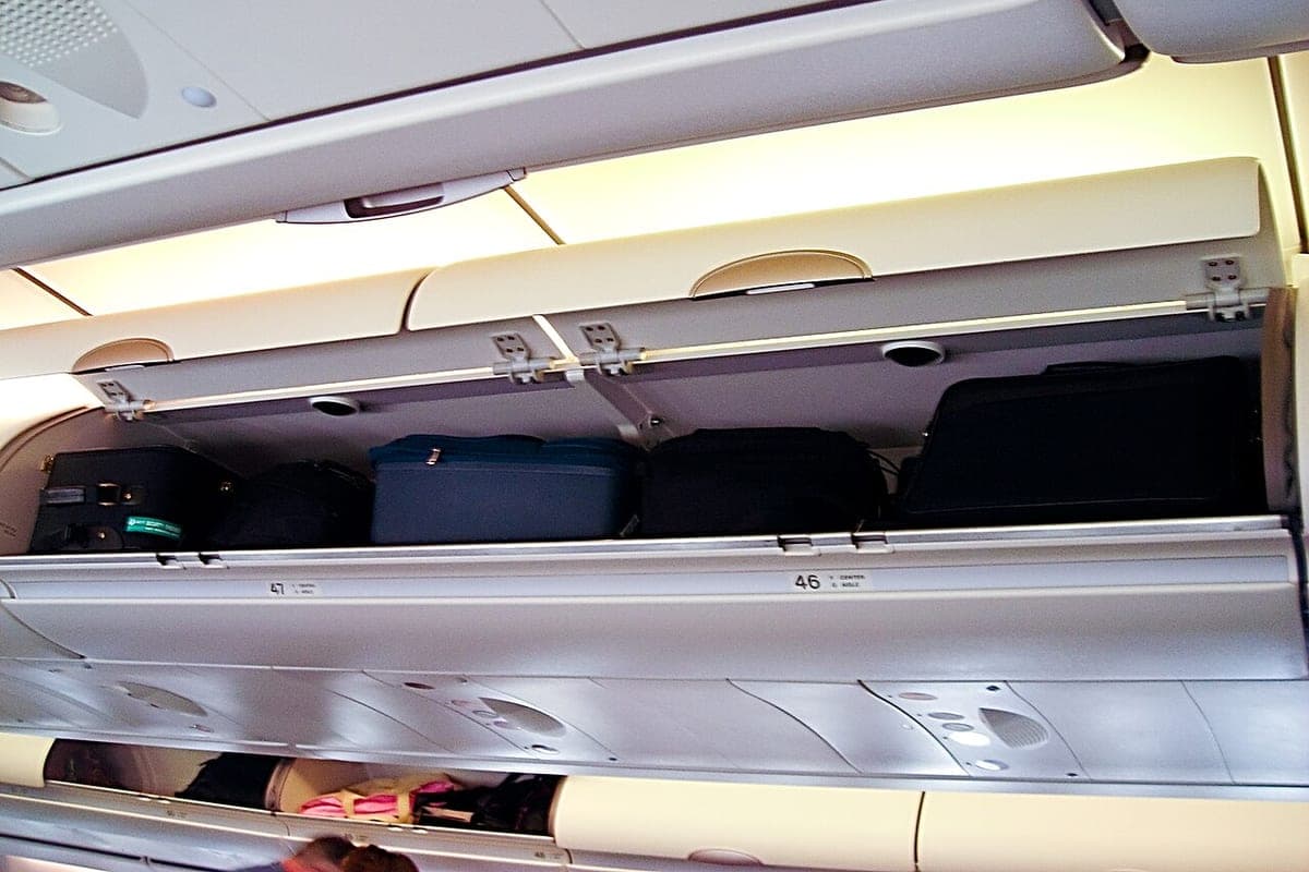 An open aircraft overhead bin with cabin bags stowed inside