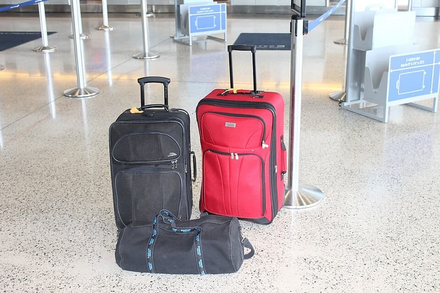 Two wheeled suitcases and a duffel bag beside a carry-on sizer at an airport