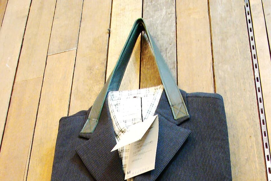 A folded suit jacket laid on a bed beside an open suitcase